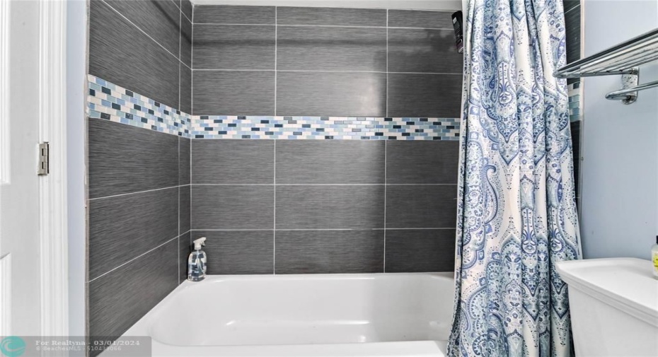 Guest bathroom has tub/shower combination with designer tile