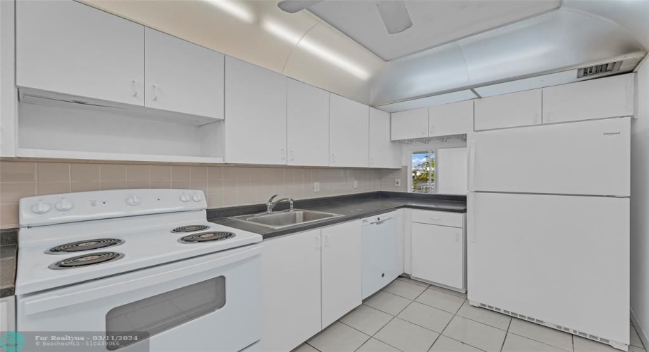 Kitchen offers white cabinets and appliances with tile flooring