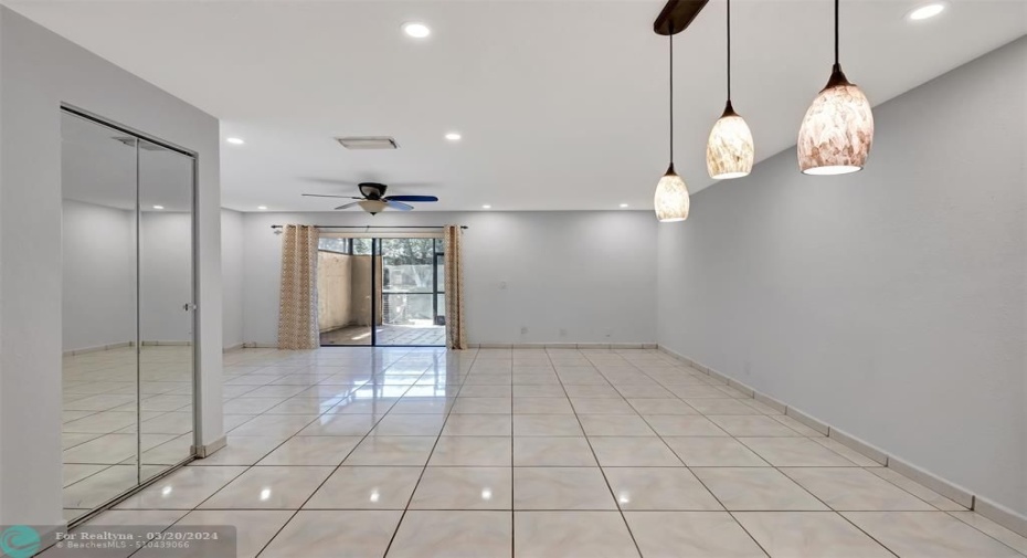 Large dining room with large under stairs storage closet to left.  Living room in distance followed by hard roofed and screened patio with storage leading to wide water view.