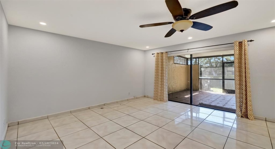 Living room area freshly painted, high hat lighting leading to tiled patio with hard covered roof and screening. Slider has shutters for storms.