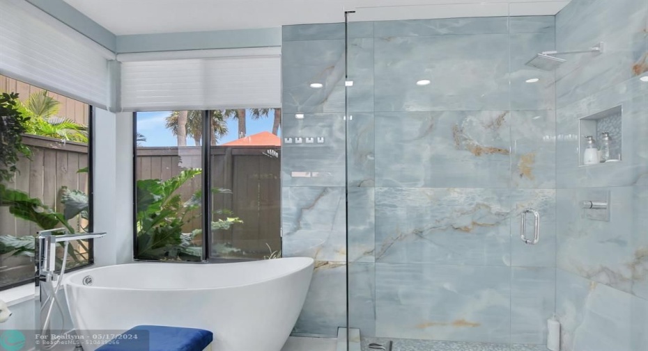 Tub is surrounded by natural light from windows. Step in shower is enclosed by frameless glass & door.