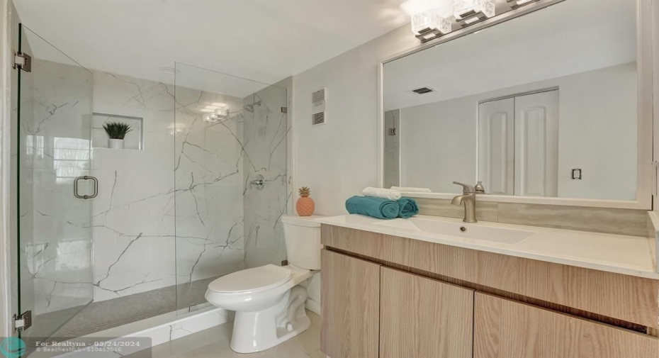 UPDATED primary bath boasts counter height vanity and frameless shower with quartz waterfall walls.